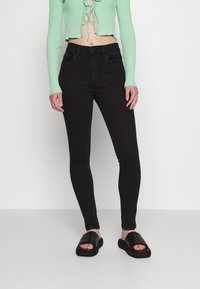Jeans skinny pretos com cintura alta, apresentando bolsos frontais e um material de denim liso e elástico. Combinados com um top cropped canelado verde menta.