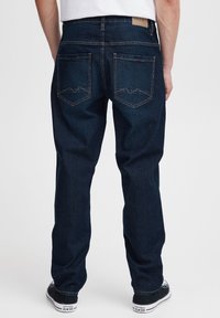 Tummansininen suoralahkeiset farkut, joissa on kaksi takataskua vuoristetulla vuoristomuotoisella ompeleella ja vyötäröllä vaaleanruskea nahkalappu.