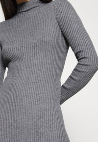 Robe en maille côtelée gris clair avec un col montant fictif, silhouette ajustée et manches longues, mettant en valeur un motif de tissu texturé.