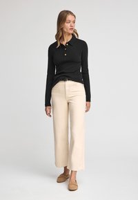 Polo a maniche lunghe nero con bottoni, abbinato a pantaloni a gamba larga beige chiaro e scarpe slip-on marroni. Design semplice e pulito.