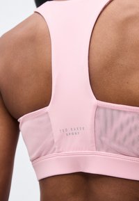 Κοντινό της επάνω πλάτης ενός ατόμου που φοράει ροζ αθλητικό σουτιέν Ted Baker Sport racerback με πλευρικά πάνελ από δίχτυ.