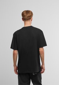 T-shirt nera in cotone con maniche corte, colletto rotondo e vestibilità comoda, vista da dietro. Nessun logo o motivo visibile.