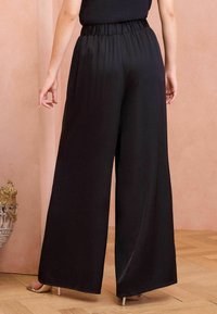 Pantaloni neri a gamba larga con vita elasticizzata, realizzati in morbido tessuto di satin, presentano una vestibilità drappeggiata e linee semplici e pulite.