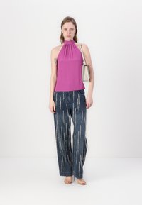 Ružový halter top s vrúbkovaným výstrihom, skombinovaný so širokými modrými denimovými nohavicami so striebornými zipsami. Modelka drží krémovú kabelku.