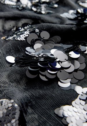 Mustast kangast, millel on tekstuurse pinnaga hallatav muster, on paigutatud läikivate mustade ja hõbedaste litrite ringikujulisi kujundeid, luues peegeldava mustri.