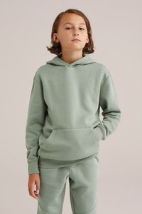 Felpa verde chiaro realizzata in un tessuto morbido, con tasca frontale, cappuccio regolabile e polsini a coste. Abbinata a pantaloni jogger coordinati.