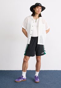 Hvit perforert kortermet skjorte, svarte shorts med grønne detaljer, lilla sneakers. Ytterligere detaljer inkluderer en svart caps med gul kant.