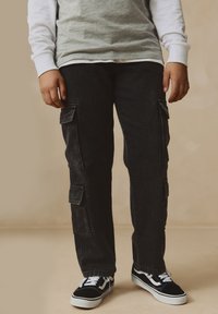 Cargo pants in black denim with knee pockets and a straight-leg fit, paired with black and white sneakers featuring white laces and a classic design.