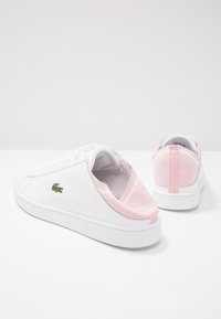 Paire de baskets blanches avec dos en tricot rose slip-on et logo crocodile vert sur le côté, présentées vues de dos et de profil.
