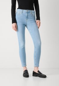 Jean skinny bleu clair avec taille haute, tissu en denim doux et peu décoloré, associés à des mocassins noirs avec une lanière décorative.