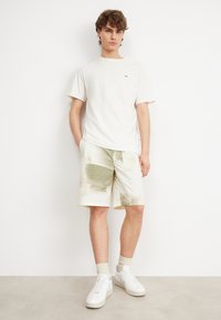 Light, plain white cotton T-shirt paired with patterned, light-colored shorts featuring grid and abstract designs; worn with white sneakers.