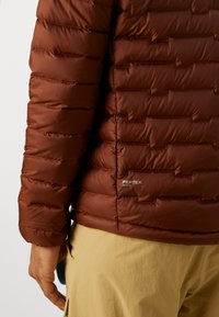 Brown insulated jacket made of Pertex fabric, featuring a quilted design with horizontal baffles, smooth texture, and logo detail on the side.