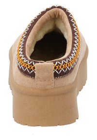 Brune og tan ruskinds slip-on sko med en tyk sål, der har dekorativ syning i orange og hvid langs kraven og en tekstureret overflade.