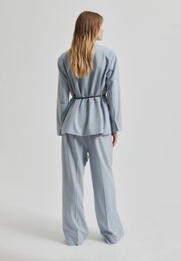 Svetlobluzni krojeni poslovni suknjič z dolgim blazerjem in peplum zadnjico ter širokimi hlačami, izdelan iz gladkega in trdnega blaga.