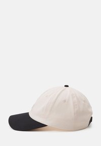 Baseball cap featuring a light beige crown and a dark navy bill. Made of cotton, with ventilation eyelets and an adjustable strap.