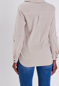 Chemise à manches longues beige clair avec un motif circulaire, dotée d'un col et de poignets boutonnés, confectionnée dans un tissu doux. Coupe décontractée indiquée.
