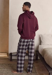 Bordeaux hoodie med en känguruficka och fastsatt huva, i kombination med svartvita rutiga pyjamasbyxor. Har en lös passform och mjuk tyg.