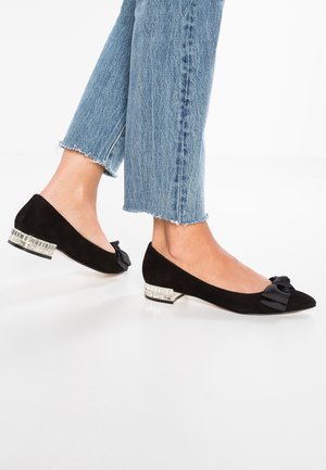 Czarne zamszowe baleriny z kokardą na palcach i niskim obcasem ozdobionym kryształkami. Noszone z niebieskimi dżinsami z postrzępionymi końcami.