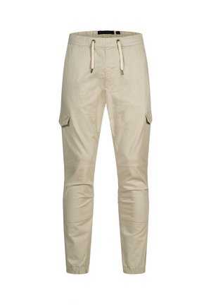 Beiget väriset slim-fit-housut kuminauhavyötäröllä, valkoisilla kiristysnarulla, sivutaskuilla ja kuminauhakupeilla nilkoissa.