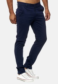 Pantalones azul marino hechos de tela ligera, con un corte ajustado, bolsillos delanteros y cierre de cremallera, combinados con zapatillas blancas.