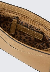 Tan nep leren interieur van een tas met een ritsvak. Gevoerd met een bruine luipaardprint stof. Zichtbare stiksels en een merklabel.