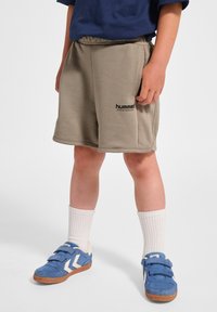 Beige sportshorts med elastisk midjeband och en svart logotyp; kombinerat med blå mockaskor med vita detaljer och vita strumpor.