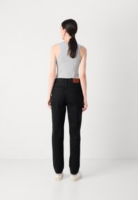 Pantaloni in denim neri con una vestibilità dritta, dotati di un'etichetta con logo sul retro e due tasche posteriori. Abbinati a un top grigio senza maniche e scarpe bianche.
