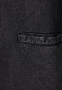 Närbild av en mörkgrå tygficka med en horisontell sprickdetalj på ett texturerat plagg.