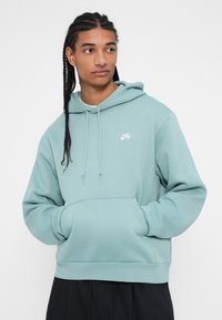 Sudadera verde menta hecha de una suave mezcla de algodón, con un bolsillo frontal, capucha con cordón y un pequeño logo blanco de Nike en el pecho.