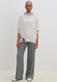 Hellgrauer, übergroßer Pullover mit einem Schalkragen, über einem eng anliegenden grauen Langarmtop getragen, gepaart mit weit geschnittenen grauen Hosen und weißen Stiefeln.