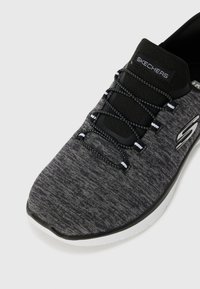 Černá a šedá sportovní bota s texturovaným vrškem, elastickými tkaničkami a bílou podrážkou. Na boku se nachází logo "Skechers".