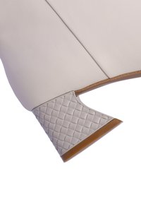 Zapato de cuero blanco con un tacón gris texturizado en un patrón de cuadrícula y una base marrón. El diseño incluye una punta redondeada y elegante.