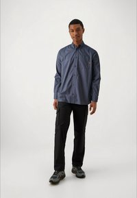 Mornarska srajca na gumb z žepom na prsih, v kombinaciji s črnimi cargo hlačami. Obleka vključuje sivo-rdeče športne copate za sproščen videz.