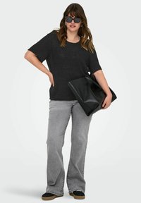 Črna oversized majica, sivi zvonasti kavbojke in črne čevlje. Model drži sijočo črno torbo. Dodatki vključujejo črne sončna očala.