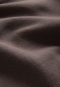 Zachte bruine stof met fijne gebreide structuur en zachte plooien die gladde, gebogen vormen en subtiele schaduwen creëren.