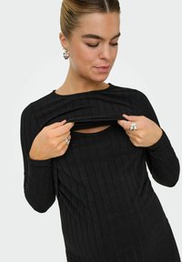 Top lungo a maniche corte nero a coste con scollo rotondo e un'apertura, che mette in risalto un design aderente e una texture morbida. Include linee verticali sottili.