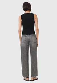 Zwarte ribbed mouwloze top gecombineerd met hoogblijvende lichtgrijze wijde jeans met contrasterende stiksels en twee achterzakken. Zwarte sandalen.