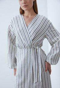 Gestreiftes Wickelkleid aus weißem und grauem Leinen, mit langen Ärmeln, tailliertem Bund und V-Ausschnitt. Vertikale Streifen sorgen für eine schmeichelhafte Passform.