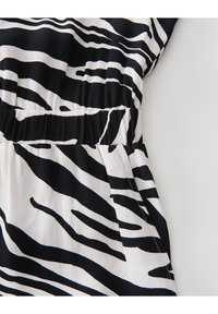 Tissu rayé noir et blanc présentant un motif de zèbre, avec une taille élastique et un matériau doux et texturé, partiellement visible.