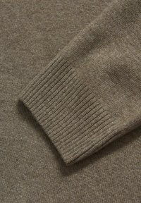 Ruskeat neulotut hihansuut, joissa on raidoitettu pinta, sileä viimeistely ja hienovaraiset värierot, luoden lämpimän ja kutsuvan ilmeen.