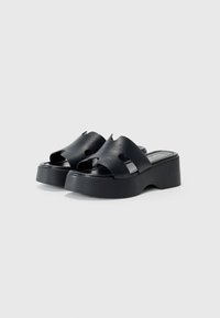 Sandalias de plataforma negras hechas de material sintético suave. Diseño de punta abierta con dos secciones recortadas y una suela gruesa.