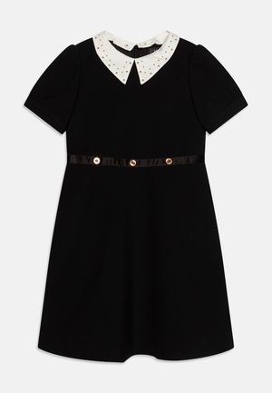 Rochie neagră cu mâneci scurte, guler alb cu studs aurii, curea din satin cu nasturi aurii și fustă evazată.