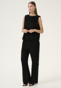 Ensemble deux pièces noir en tissu texturé et duveteux ; haut sans manches et pantalon large. Design minimaliste sans motifs ni accents visibles.