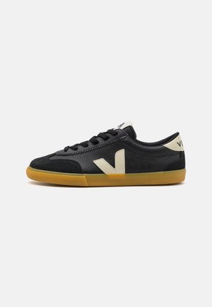 Baskets basses noires avec logo "V" beige, semelle en gomme, lacets noirs et languette de talon beige sur fond blanc uni.