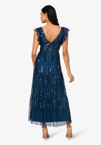 Lange, marineblauwe jurk met een V-rug, voorzien van gerimpelde schouderbanden en paillettenaccenten. Vloeiende silhouette met gelaagde textuur.