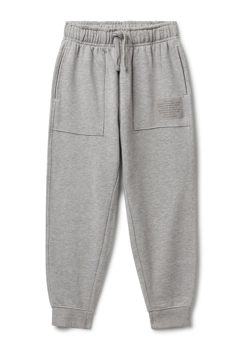 Hellgraue Trainingshose mit elastischem Bund, Kordelzug, großen Fronttaschen, Bündchen an den Knöcheln und einem kleinen Textpatch auf der rechten Tasche.