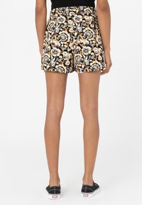 Shorts noirs avec motif floral orange et blanc, taille élastique et coupe décontractée. Portés avec des chaussures noires et un haut simple.