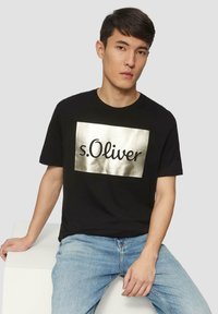 Zwarte katoenen t-shirt met een metallic zilveren rechthoekige grafiek met de tekst "s.Oliver" in een cursieve lettertype. Casual fit.