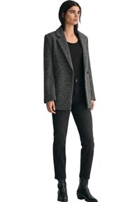 Svart och grått hundtandsmönstrat blazer med slag, dubbelknäppt front och textilmaterial, i kombination med svarta jeans och ankelskor.