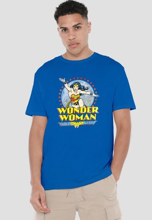 Young man wearing a blue Wonder Woman T-shirt with comic-style character and yellow text, paired with beige cargo shorts.